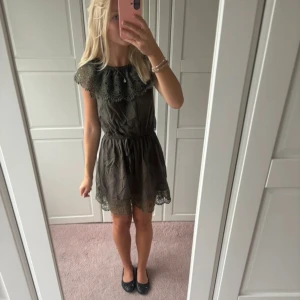 Mörkgrön kortklänning med spets - Supersöt mörkgrön klänning med spetsdetaljer vid axlar och nederkant. Modellen är kort med ett elastiskt midjeband som ger en snygg siluett. Klänningen är ärmlös och har en rund halsringning som även går att göra of shoulder med dekorativ spets. Lånade bilder!!