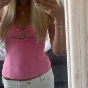 Rosa korsettopp med rosetter - Supersöt rosa korsettopp med smala axelband och två dekorativa rosetter framtill. Toppen har en liten cut-out mellan rosetterna som ger en extra detalj. Toppen är i storlek xs, skriv om du har frågor! Använd en gång!