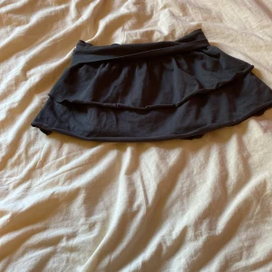 Grå volangkjol från H&M - Grå kortkjol från H&M med dubbla volanger och bred resår i midjan. Kjolen är gjord i mjuk bomull med lite stretch för extra komfort. Perfekt för dig som gillar en enkel men ändå söt stil.