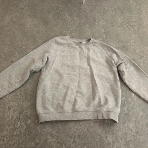 Grå sweatshirt från H&M  - En enkel och stilren grå sweatshirt från H&M i storlek XS. Tröjan har rund hals, långa ärmar och ribbade muddar vid ärmslut och nederkant. Regular fit som sitter skönt och passar till chill dagar. Perfekt att matcha med jeans eller mjukisbyxor.