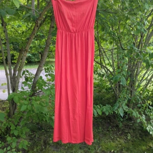 Orange/röd långklänning från H&M Basics - Snygg röd/orange långklänning från H&M Basics i storlek L. Klänningen är axelbandslös med rak överdel och har en mjuk, flowy passform. Tillverkad i en skön mix av bomull och modal som känns lätt och sval mot huden. Perfekt för varma dagar och chill häng utomhus. Katter finns i hemmet.