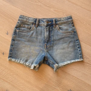 Jeansshorts med fransig kant Kappahl - Snygga blå jeansshorts från Kappahl med fransig kant nertill och klassisk femficksmodell. Shortsen har normal passform och är perfekta för varma sommardagar. Tillverkade i slitstarkt jeanstyg med cool tvättad look.