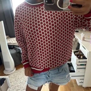 Röd mönstrad tröja med vita hexagoner - Säljer en röd tröja med coolt hexagonmönster i vitt. Tröjan har rund hals och ribbade muddar med vita och svarta ränder vid hals och ärmslut. Passformen är normal och materialet känns mjukt och skönt mot huden. Perfekt för dig som gillar grafiska mönster!