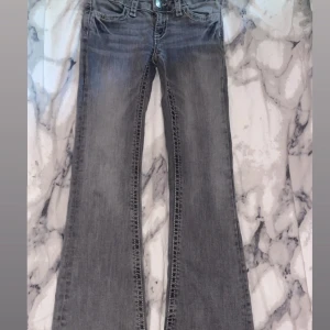 Grå bootcut jeans med kontrastsömmar - Snygga grå jeans från Ginatricot med bootcut-modell och markerade vita kontrastsömmar. Jeansen har fem fickor, coola bakfickor med lock och knapp samt klassisk knappgylf. Perfekta för dig som gillar en avslappnad men trendig look.