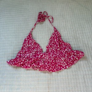 Rosa leopardmönstrad bikini från Joress - Supersöt bikiniöverdel från Joress i rosa och vitt leopardmönster. Modellen har volangkant nedtill och knyt i nacken och ryggen för perfekt passform. Tunn och lätt i materialet, perfekt för strandhäng och soliga dagar.