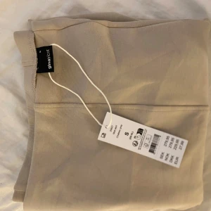 Beige långkjol från Gina Tricot - Snygg beige långkjol från Gina Tricot i storlek S aldrig använt o prislapp kvar. Kjolen har en rak och enkel design med bred linning och är tillverkad i ett mjukt och lätt material som känns skönt mot huden. Perfekt för dig som gillar stilrena och neutrala plagg.