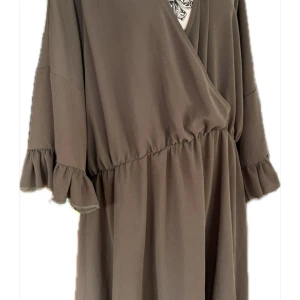 Brun omlottklänning från Boohoo - Säljer en brun omlottklänning från Boohoo med volangdetaljer på de halvlånga ärmarna och markerad midja. Klänningen har v-ringad hals och är tillverkad i ett mjukt, lätt polyestertyg som faller snyggt. Perfekt för dig som gillar avslappnad men chic stil.