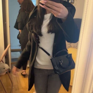 Svart kappa med krage - Snygg svart kappa med klassisk krage och knäppning framtill. Jackan har en rak passform och är perfekt för kyligare dagar. Stilren design som funkar till många outfits. Långärmad och i ett mjukt material som känns bekvämt.