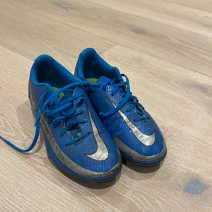 Nike Phantom blå fotbollsskor - Säljer ett par Nike Phantom fotbollsskor i blått med silverfärgade detaljer och snörning. Skorna har en sportig look med rund tå och är tillverkade i syntetmaterial. Perfekta för dig som älskar fotboll och vill sticka ut på planen.