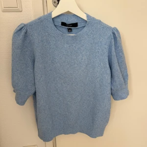 Ljusblå stickad tröja med puffärm - Superfin ljusblå stickad tröja från Vero Moda med korta puffärmar och rund hals. Tröjan har ribbade muddar vid ärmslut och nederkant, vilket ger en snygg och modern look. Perfekt för dig som gillar mjuka material och trendiga detaljer.