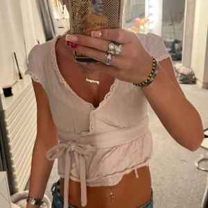 Ljusrosa omlottopp - Supersöt ljusrosa omlottopp från SHEIN med knyt i midjan och fina spetsdetaljer längs kanterna. Toppen är croppad och har korta ärmar med vågig kant. Perfekt för dig som gillar romantisk och feminin stil.