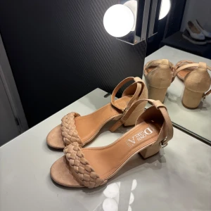 Beige klackar med flätad rem  - Snygga klackar i beige mocka-look med flätad rem över tårna och justerbart spänne runt ankeln. Skorna är endast använda ett fåtal gånger och nypris är 599kr💛💛