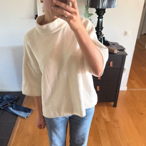 Vit polotröja med korta ärmar - Säljer en vit polotröja med korta, vida ärmar och lös passform. Tröjan har en mjuk, frottéliknande yta och hög krage som ger en chill och modern vibe. Perfekt att styla med jeans eller kjol för en clean look.