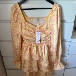 Gul blommig volangklänning med puffärm - Superfin gul klänning från Andrea Norrman X Bubbelroom  med rosa blommönster, volanger och puffiga armar. Klänningen har lappen kvar och är aldrig använd.