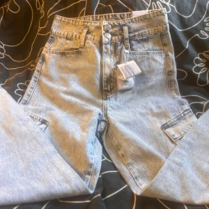 Ljusblå cargo jeans från Amisu, stl 36 - Snygga ljusblå cargo jeans från Amisu i storlek 36. Byxorna har hög midja, raka ben och coola cargofickor på sidorna. Tillverkade i klassiskt denim med dubbla knappar i midjan. Perfekta för en avslappnad streetstyle-look.