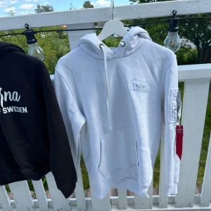 Vit hoodie alpha industries  - Hoodie från alpha industires med tryck på ryggen och vitt märke på bröstet