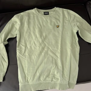 Ljusgrön sweatshirt från Lyle & Scott - Snygg ljusgrön sweatshirt från Lyle & Scott Junior med klassisk rund hals och broderad gul fågel på bröstet. 