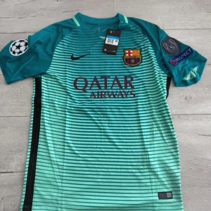 FC Barcelona Neymar Jr bortatröja - Snygg FC Barcelona bortatröja från Nike med Neymar Jr och nummer 11 på ryggen. Tröjan är turkos med svarta tunna ränder, gula detaljer och klubbmärke på bröstet. Korta ärmar, Champions League-patch och Qatar Airways-tryck framtill. Tillverkad i lätt och ventilerande material.