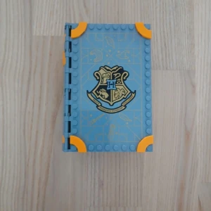 Hogwarts LEGO Bok - Cool bok i LEGO-format med Hogwarts-emblem och minifigurer som liknar karaktärer från en magisk värld. Perfekt för dig som älskar byggsatser och vill ha något unikt i bokhyllan. Passar både som samlarobjekt och lekset för unga fans. Skriv privat för fler bilder eller prisförslag.