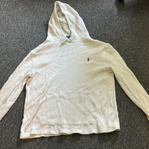 Vit hoodie från Polo Ralph Lauren - Säljer en vit hoodie från Polo Ralph Lauren i storlek L. Tröjan har ett diskret rutmönster i materialet, huva med snörning och en klassisk känguruficka framtill. Liten broderad logga på bröstet. Den sitter lite slappt runt midjan. Skicka pm för frågor