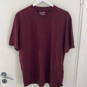 Vinröd t-shirt från Jack & Jones - Snygg vinröd t-shirt från Jack & Jones med diskret logga tryckt på bröstet. Klassisk rund hals och korta ärmar. Tillverkad i mjuk bomull som känns skön mot huden. Perfekt för dig som gillar enkel och stilren design.