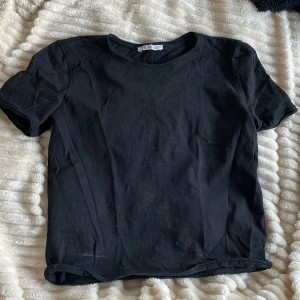 Svart basic t-shirt från Zara - En svart, enkel t-shirt från Zara  med rund hals och korta ärmar. Modellen är klassisk och har en normal passform, perfekt till jeans eller shorts. Den har ett fint veck vid ryggen som ger en fin twist till ett vardagligt plagg. (Den ser bättre ut på)💗💗den är liten i storleken