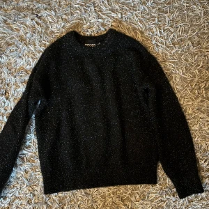 Svart glittrig tröja från Pieces - Säljer en svart glittrig tröja från Pieces i storlek XS. Tröjan har lång ärm och en klassisk rund halsringning. Materialet är mjukt och har en skimrande finish som ger en snygg touch. Perfekt för dig som gillar att sticka ut med lite glitter i vardagen.