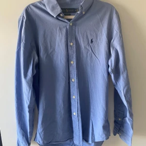 Ralph Lauren skjorta - Klassisk ljusblå skjorta från Ralph Lauren i slim fit-modell. Skjortan har långa ärmar, knappar framtill och den ikoniska broderade loggan på bröstet. Tillverkad i bomull och passar perfekt till en stilren look.