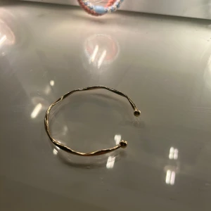 Guldigt vridet armband - Snyggt armband i guldig metall med vriden design och små kulor i ändarna. Enkel men trendig accessoar som passar perfekt till din vardagsstil eller när du vill addera lite extra till outfiten.