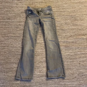 Grå bootcut jeans med låg midja - Säljer ett par grå jeans med bootcut-modell och låg midja. Jeansen har klassiska fem fickor och snyggt slitna detaljer. Perfekta för dig som gillar en avslappnad men ändå trendig look.