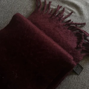 Vinröd halsduk från H&M Divided - Mysig och lång vinröd halsduk från H&M Divided. Halsduken är enfärgad, har en fluffig känsla och fransar i ändarna. Perfekt att vira flera varv runt halsen för extra värme. Tillverkad i 100% polyester och mäter 220x27 cm.