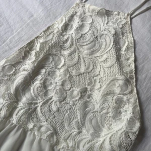 Vit spetsklänning från Ivyrevel - Supersöt vit kortklänning från Ivyrevel med tunna axelband och spets upptill. Klänningen har ett blommigt spetsmönster på överdelen och ett lätt tyg nedtill. 