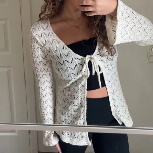 Gina tricot kofta - Säljer en beige stickad omlottopp med lång ärm och snygg knytning framtill. Toppen har ett öppet mönster med zigzag-detaljer och v-ringad hals. Perfekt för dig som gillar boho-vibes och vill ha något luftigt och trendigt till sommaren.