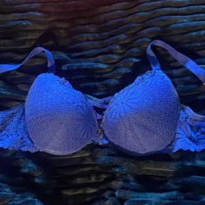 Blå spetsig BH med snörning från juicy couture  - Aldrig använd, köpt för 799kr i butik i USA. Säljer en blå korsettopp från juicy couture med vadderade kupor och snygg spetsdetalj över hela framsidan. Toppen har snörning mellan kuporna och ett metallhänge framtill. Axelbanden är justerbara och har text ”juicy couture” på sig,  spetsen har ett blommigt mönster.