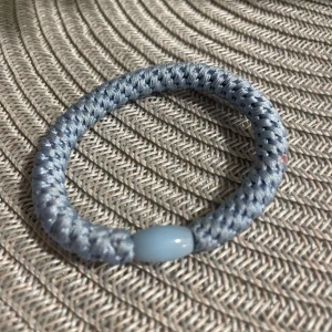 Blått flätat armband med pärldetalj - Snyggt armband i ljusblått med flätad design och en oval pärldetalj i plast. Armbandet har en sportig och enkel look som passar perfekt till en avslappnad stil. Materialet är mjukt och bekvämt mot huden.