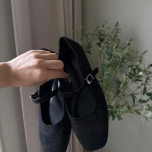 Svarta ballerinaskor mocka - Stilrena svarta ballerinaskor från 157 i mjuk mocka med klassiskt spänne över foten. Skorna har platt sula och rundad tå, perfekta för en chic och enkel look. Passar till både jeans och klänning. (Oanvänd)