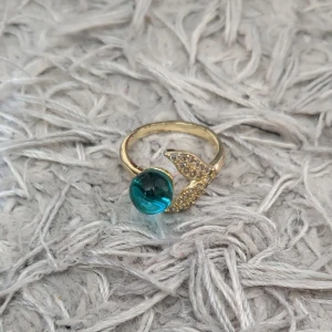 Ring - Unik guldfärgad ring med en stor blå rund sten och glittriga små stenar på ena sidan. Ringen har en modern och cool design som verkligen sticker ut. Perfekt för dig som vill ha något annorlunda och snyggt på fingret. Går att göra mindre och större☺️