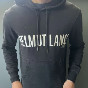 Helmut Lang hoodie - Svart Helmut Lang hoddie med tryck på bröstet. Två små hål som knappast syns på sidorna av magfickan (se bild)
