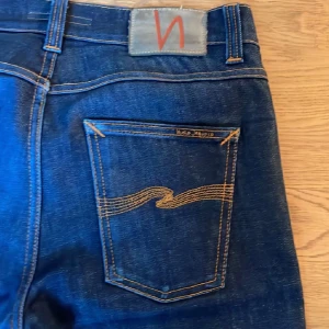 Mörkblå slim jeans från Nudie - Snygga mörkblå jeans från Nudie med klassisk gul söm och tillverkad i slitstarkt bomullsjeans. Perfekta för dig som gillar stilren look.