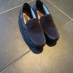 Mörkblå mockaloafers från Zeus - Snygga mörkblå loafers från Zeus i mjuk mocka med kontrasterande vita sömmar. Skorna har en klassisk design med rund tå och bekväm innersula. Perfekta för en stilren och avslappnad look. Dom är i storlek 43 men passar 44. Använda en gång på min bal sen inte använda nått mer. Ny pris är 1000kr. Box medföljer!