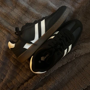 Svarta och vita sneakers från Lejon - Snygga svarta sneakers från Lejon med vita detaljer och klassiska ränder på sidorna. Skorna har snörning, platt sula i gummi och rund tå. Perfekta för dig som gillar en sportig och stilren look. Storlek 39 men passar även för de med storlek 40 eller 38. Har aldrig använts innan så den är garanterat helt ny. 