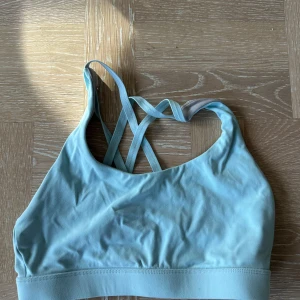 Ljusblå sportig linnetopp - Säljer en ljusblå linnetopp med smala korsade axelband i ryggen. Perfekt för träning eller chill dagar. Mjuk och stretchig känsla, sitter skönt mot kroppen och ger bra stöd. Enkel och stilren design som passar till det mesta.
