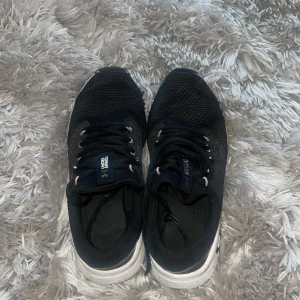 Svarta Under Armour sneakers - Svarta sneakers från Under Armour med vit sula och klassisk snörning. Ovandelen är i mesh-liknande syntetmaterial som andas och har diskreta mönsterdetaljer på sidorna. Perfekta för träning eller en sportig vardagslook.