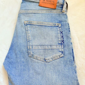 Ljusblå jeans från Scotch & Soda - Säljer ett par ljusblå jeans från Scotch & Soda med klassisk femficksdesign och snygg detaljsöm vid bakfickan. Jeansen har rak passform och är tillverkade i bomullsdenim. Perfekta för en avslappnad och trendig look. Storlek 28/32