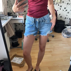 Blå jeansshorts - Snygga blå jeansshorts från Lager 157 i storlek XXS. Splitternya, endast testade med lapparna kvar. Modellen är lågmidjad med klassisk femficksdesign och rå, fransig kant nedtill för en avslappnad vibe. Perfekta för varma sommar dagar och lätta att matcha med allt. Dragkedja och knapp framtill. 