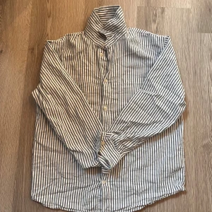 Randig skjorta från H&M i bomull - Snygg skjorta från H&M i vitt och blått med klassiskt randigt mönster. Skjortan har långa ärmar, knappar framtill och en bröstficka. Tillverkad i mjuk bomull som känns skön mot huden. Perfekt för dig som gillar en clean och stilren look.🙌🤝