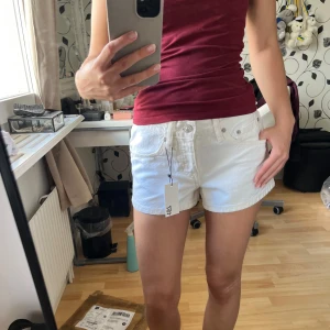 Vita broderade shorts - Snygga vita shorts från Lager 157 med broderade detaljer på bakfickorna. Splitternya shorts med prislappen kvar. Klassisk femficksmodell med knappar hela vägen ner. Perfekta för sommaren och lätta att matcha med allt. 