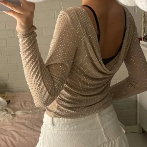 Beige mesh topp med pärlor från Zara - Superfin beige mesh topp från Zara med långa ärmar och öppen rygg. Toppens tyg är täckt av små pärlor som ger en glittrig effekt. Den har en draperad rygg (om man har den som jag har, jag har den bak och fram) och sitter tight men stretchigt. Perfekt för dig som vill sticka ut med en unik och trendig look.