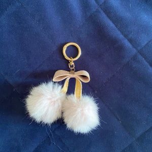 Nyckelring med fluffiga bollar och rosett - Supergullig nyckelring med två stora, fluffiga rosa bollar i fuskpäls och en rosett. Metallringen är i guldton och ger en lyxig känsla. Perfekt att hänga på väskan eller nyckelknippan för en söt detalj.