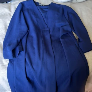 Mörkblå omlottklänning från COS - Snygg mörkblå omlottklänning från COS i storlek 44. Klänningen har trekvartsärm och en stilren v-ringning. Den har en loose passform och är perfekt för dig som gillar minimalistisk design och rena linjer.